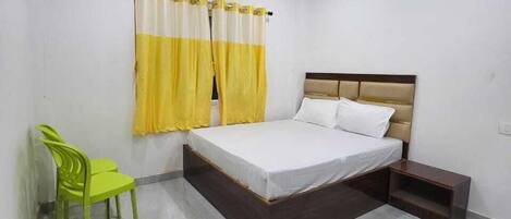 A bedroom with a bed, a chair, a nightstand, and an air conditioning unit.