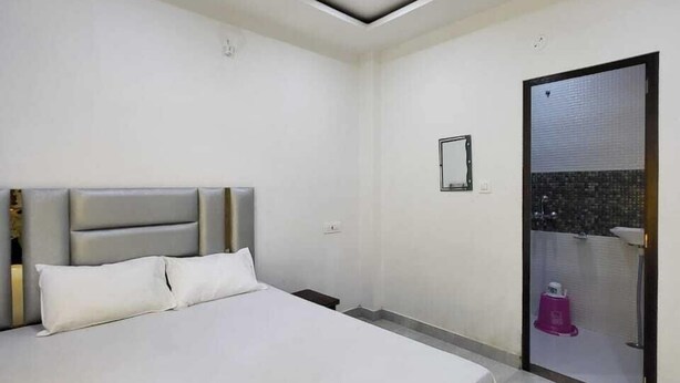 A modern bedroom with a large bed, a ceiling fan, and a bathroom visible through a glass door. - Shekhar Palace (Varanasi)