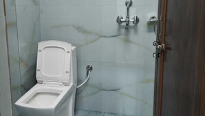A small, enclosed bathroom with a toilet, a shower, and a door. - Shekhar Palace (Varanasi)