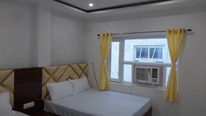A bedroom with a bed, a window with curtains, an air conditioning unit, and a ceiling fan. - Shekhar Palace (Varanasi)