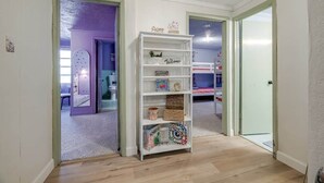 A hallway with a white bookshelf, a door, and a room with a purple wall and a bunk bed. - Bloomingdale - Mesa A - Retro! - 4BR Near Sav Airport (Bloomingdale)