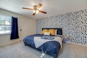 A bedroom with a bed, a ceiling fan, a window with curtains, and a patterned wall.