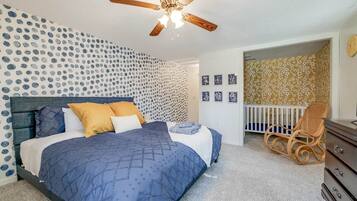 Een slaapkamer met een bed, een plafondventilator, een babybedje en een dressoir.
