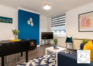 Uma sala de estar moderna com parede azul de destaque, televisão de tela plana, mesa de jantar e sofá.