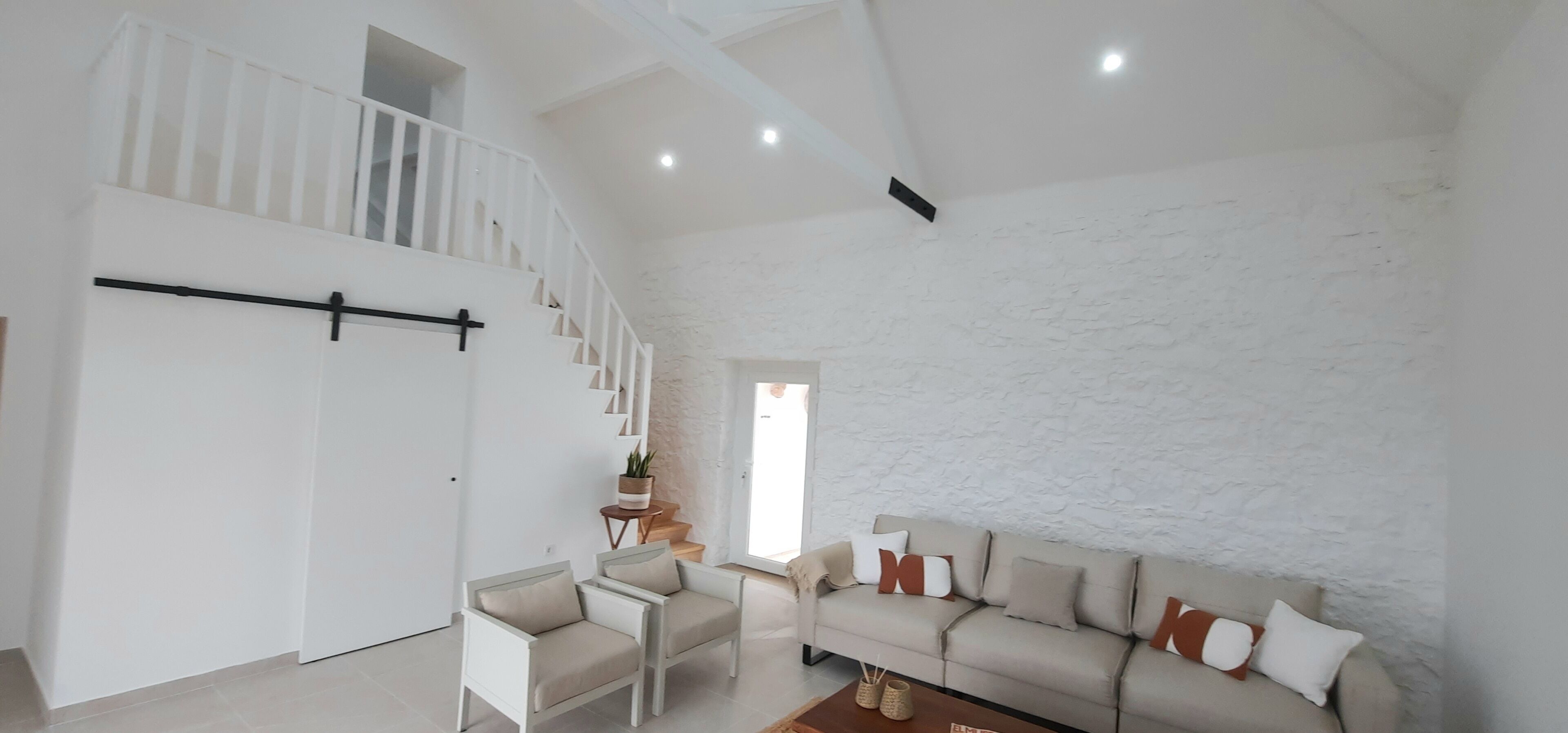 Un'ampia zona giorno con soffitto alto, una scala, un divano e un piccolo tavolino con oggetti decorativi.