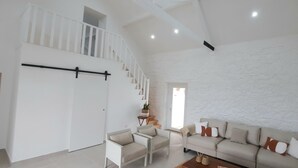 Zona d'estar àmplia amb un sostre alt, una escala, un sofà i una taula petita amb objectes decoratius.