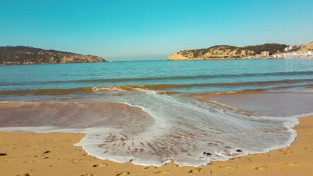 Una platja amb aigua turquesa cristal·lina, sorra daurada i turons a la distància.