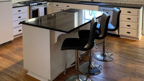 Een moderne keuken met witte kasten, een centraal eiland met barstoelen, roestvrijstalen apparatuur en een plafondventilator.