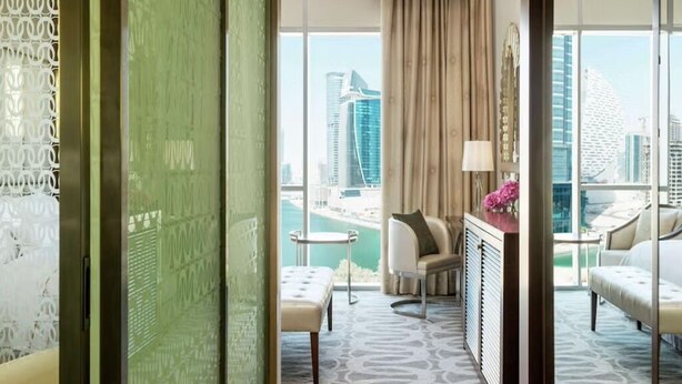 Ein Hotelzimmer mit Blick auf die Stadt, inklusive Sofa, Sessel, kleinem Tisch und einem dekorativen Spiegel.
