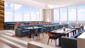Ein modernes Restaurant mit hohen Decken und großen Fenstern, das einen Blick auf die Stadt bietet.