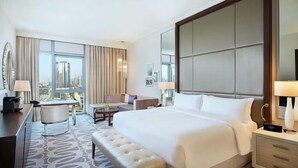 Ein Hotelzimmer mit einem großen Bett, einem Schreibtisch mit Stuhl, einer Couch und Blick auf die Stadt durch große Fenster.