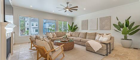 A spacious living room with a sectional sofa, a wooden rocking chair, and a large potted plant.