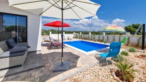 A modern outdoor pool area with a white umbrella, red and multicolored umbrellas, and lounge chairs.