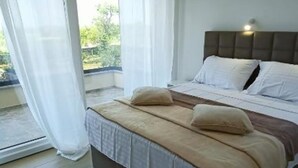 A bedroom with a bed, curtains, and a view of greenery outside.