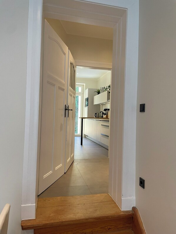 A narrow hallway leading to a kitchen with white cabinets and a wooden floor. - Chic terrace apartment with private parking space Box spring bed TV WLAN (Leipzig)
