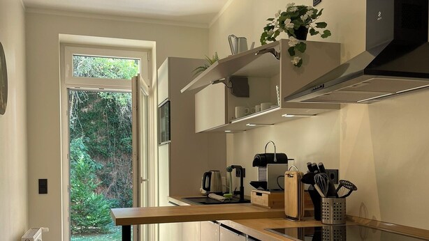A modern kitchen with white cabinetry, a wooden countertop, and a built-in stove. There is a window with a view of greenery outside. - Chic terrace apartment with private parking space Box spring bed TV WLAN in Leipzig (Leipzig)
