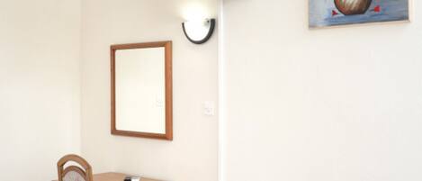 A room with a TV mounted on the wall, a framed mirror, a small wooden desk, and a chair.