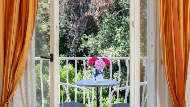 Un balcón con sillas blancas y una mesa pequeña con un florero.