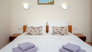 Habitación de hotel con cama, dos mesitas de noche, un cuadro de una playa y dos lámparas de pared.