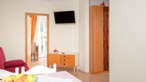 A room with a bed, a TV mounted on the wall, a wooden wardrobe, and a small table with fruit. - Apartments Božica - Studio (Vrboska)