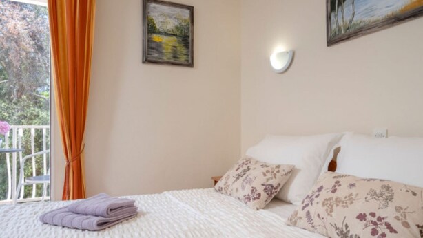 A bedroom with a bed, pillows, a painting, and a window with curtains. - Apartments Božica - Studio (Vrboska)