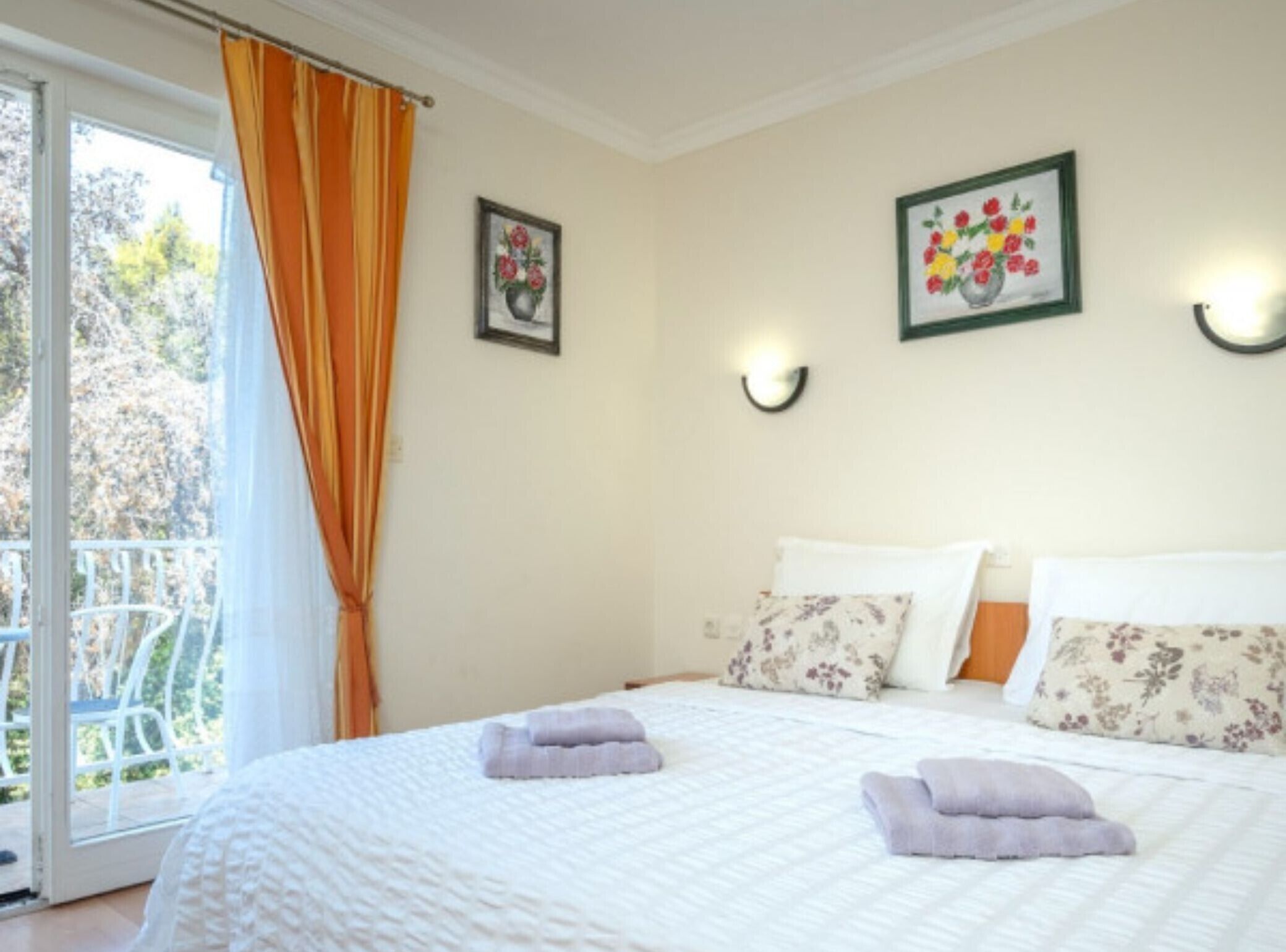 A hotel room with a bed, two pillows, a window with curtains, and two wall-mounted lights.