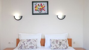 Een tweepersoonsbed met kussens met bloemenprint, een lijstwerk met bloemmotieven erboven en twee wandlampen.