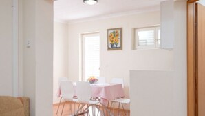 Een eetruimte met een tafel gedekt voor vier personen, witte stoelen en een schilderij van zonnebloemen aan de muur.