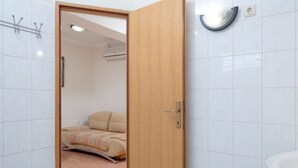 Hotelkamer met een houten deur, een bed met een beige en roze gewatteerd sprei, en een witte betegelde muur met een wandlamp.