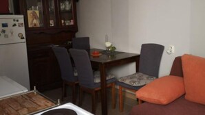 A compact living space with a dining table, four chairs, a sofa, a clock, and a kitchen area with a refrigerator and a wooden cabinet. - Apartments Roma - One Bedroom Apartment (Stanici)