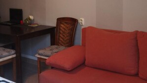 A living room with a red sofa, a wicker chair, and a small table with a lamp and a book. - Apartments Roma - One Bedroom Apartment (Stanici)