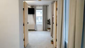 Um corredor com piso plano, uma televisão fixada na parede e um vaso de plantas.
