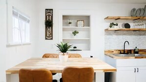 Uma cozinha moderna com uma mesa de madeira, duas cadeiras castanhas, um armário branco e uma prateleira com objetos decorativos.