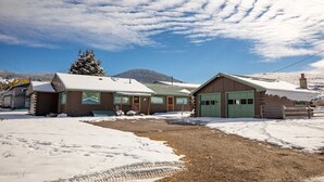A cabin-style building with a green garage door, surrounded by snow-covered ground and a clear sky.