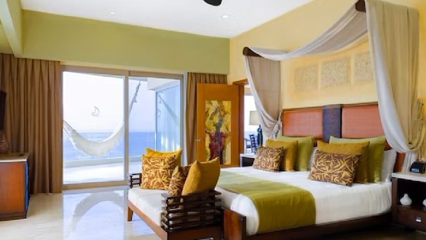 A spacious bedroom with a large bed, a nightstand, and a view of the sea through a sliding glass door.