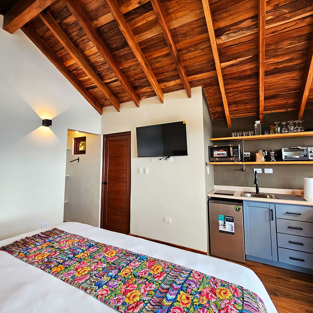Una habitación con cama, televisión, kitchenette y techo de madera.