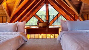 Een slaapkamer met twee bedden, een hangstoel en een groot raam met uitzicht op groen.