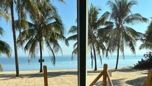 Vista a la playa a través de una ventana, con piso de madera y un felpudo con un mensaje.