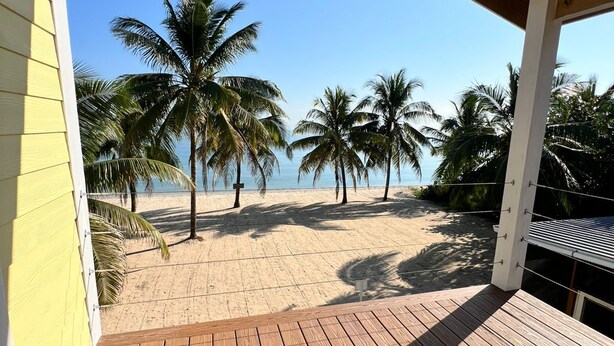 Una terraza de madera con vistas a una playa de arena y palmeras.