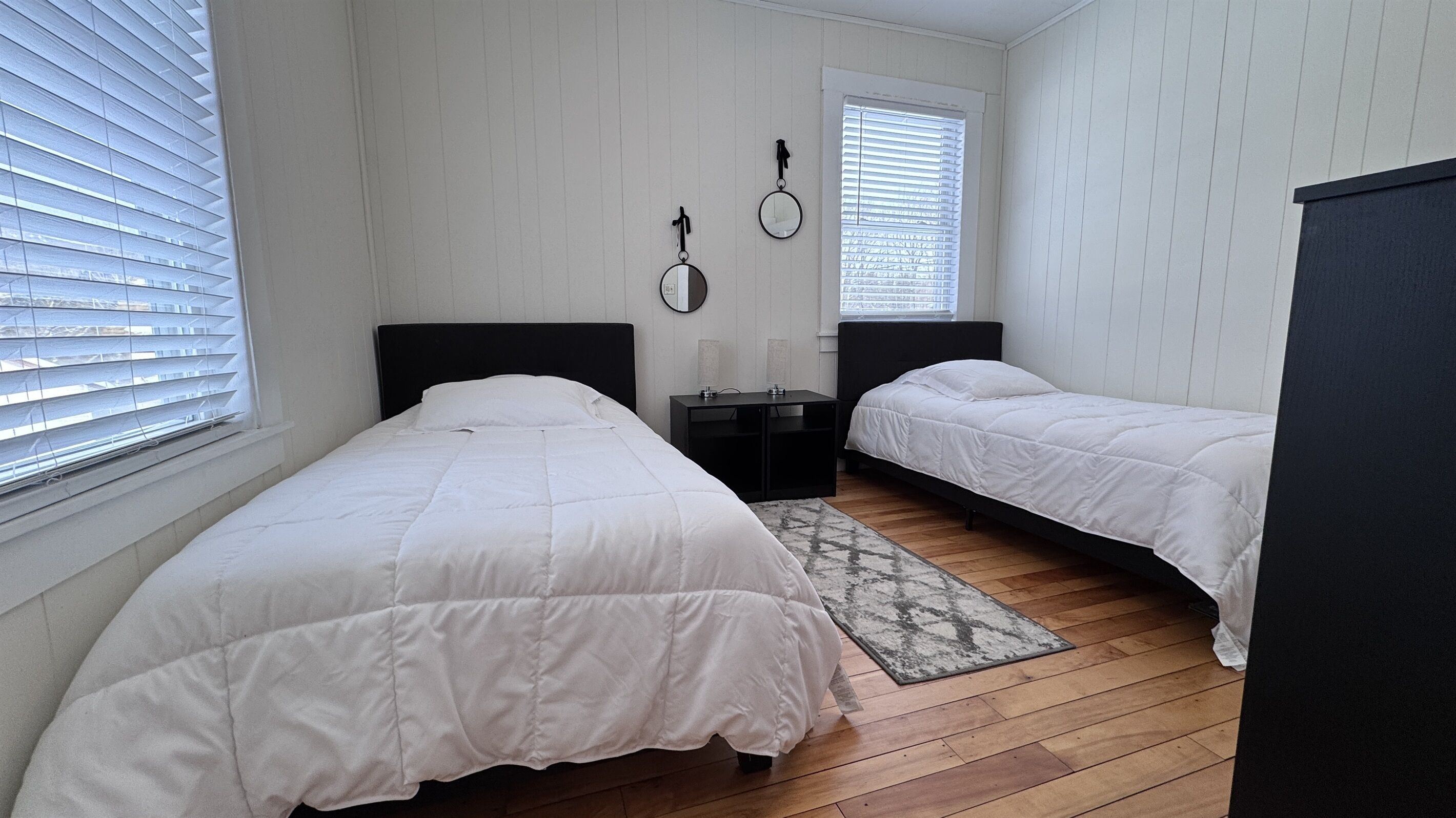 A bedroom with two single beds, a small table, and a mirror on the wall.