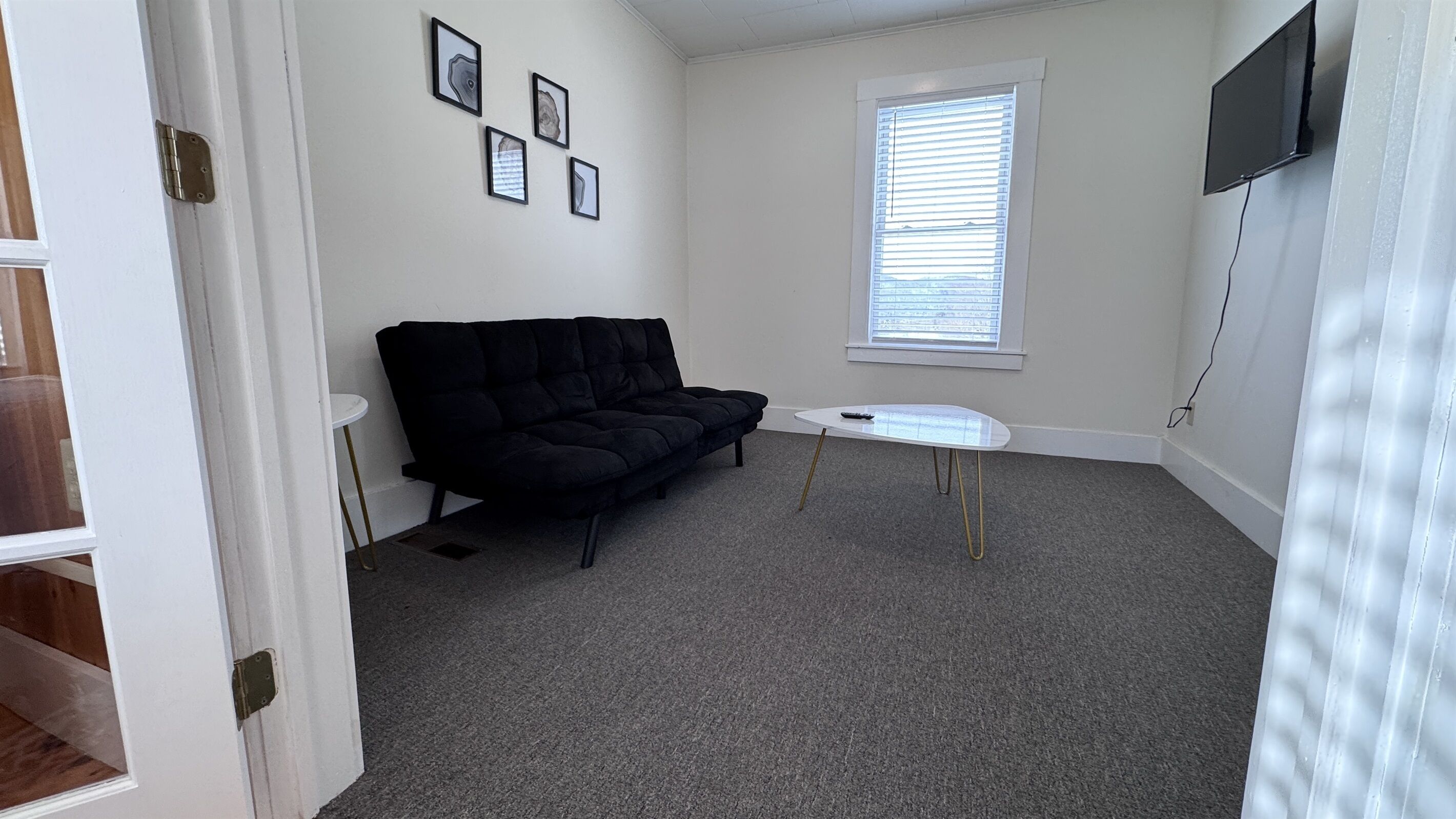 A room with a black sofa, a small white table, and a window with blinds.