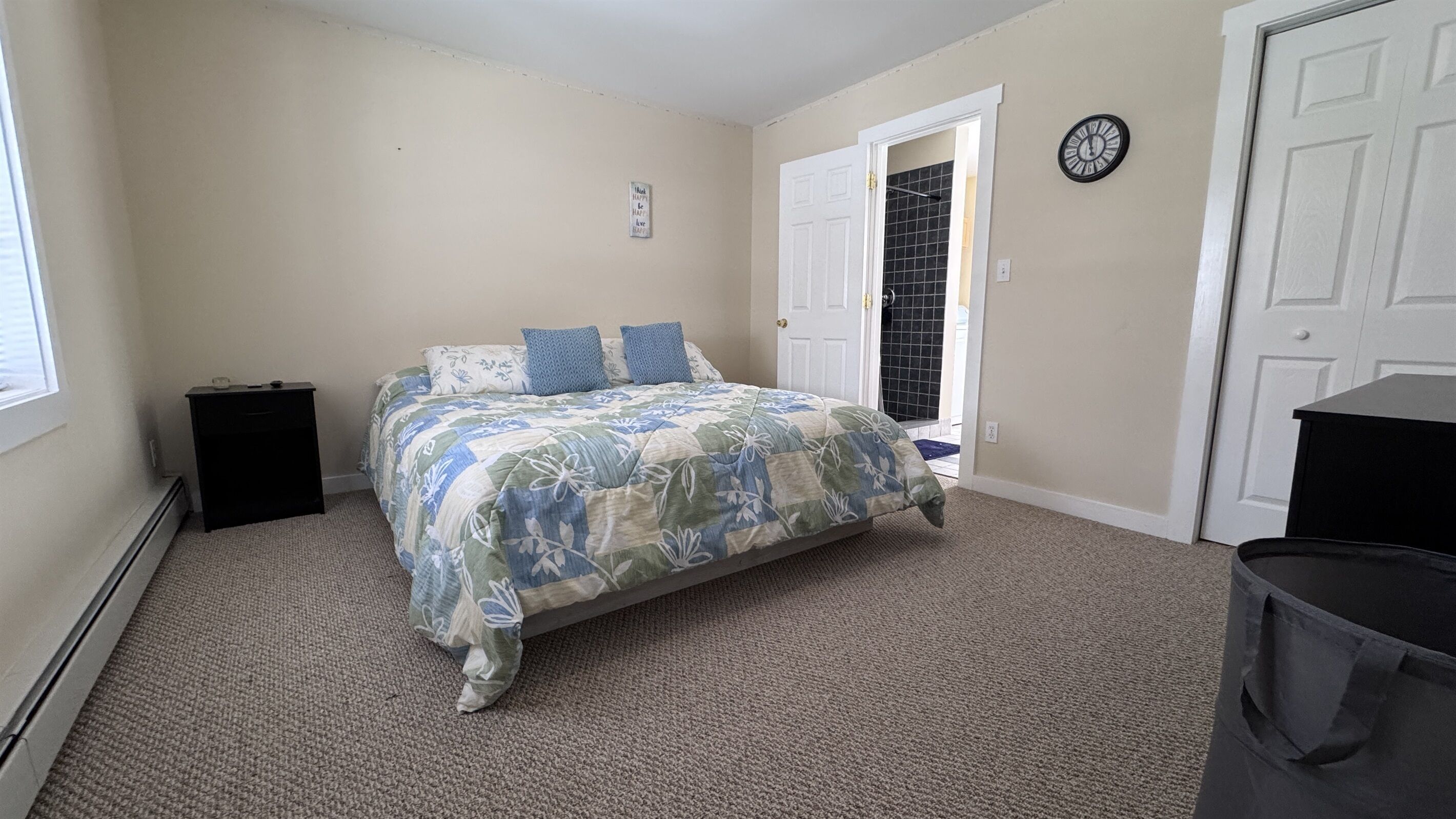 A bedroom with a bed, a nightstand, a clock, and a door.