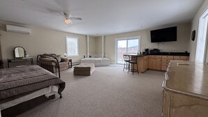 A spacious bedroom with a large bed, a sitting area with a sofa and chairs, a small kitchenette, and a bathroom with a bathtub. - Island Pond Apartment on VAST Trail – 3BR, 2BA (Brighton)