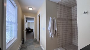 A hallway with a tiled shower area, a door leading to a bathroom, and a window with blinds. - Island Pond Apartment on VAST Trail – 3BR, 2BA (Brighton)