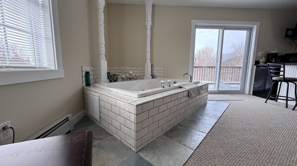 A bathroom with a large bathtub, a window, and a door leading to a balcony. - Island Pond Apartment on VAST Trail – 3BR, 2BA (Brighton)