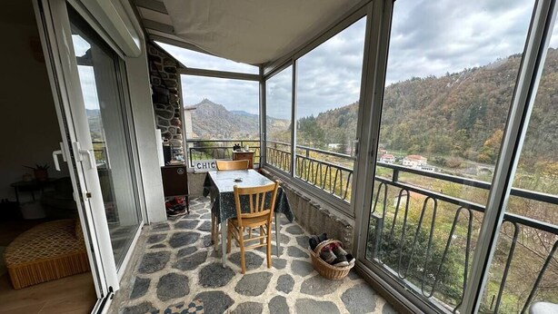 Een balkon met een stenen vloer, een tafel met stoelen en een uitzicht op een bergachtig landschap.