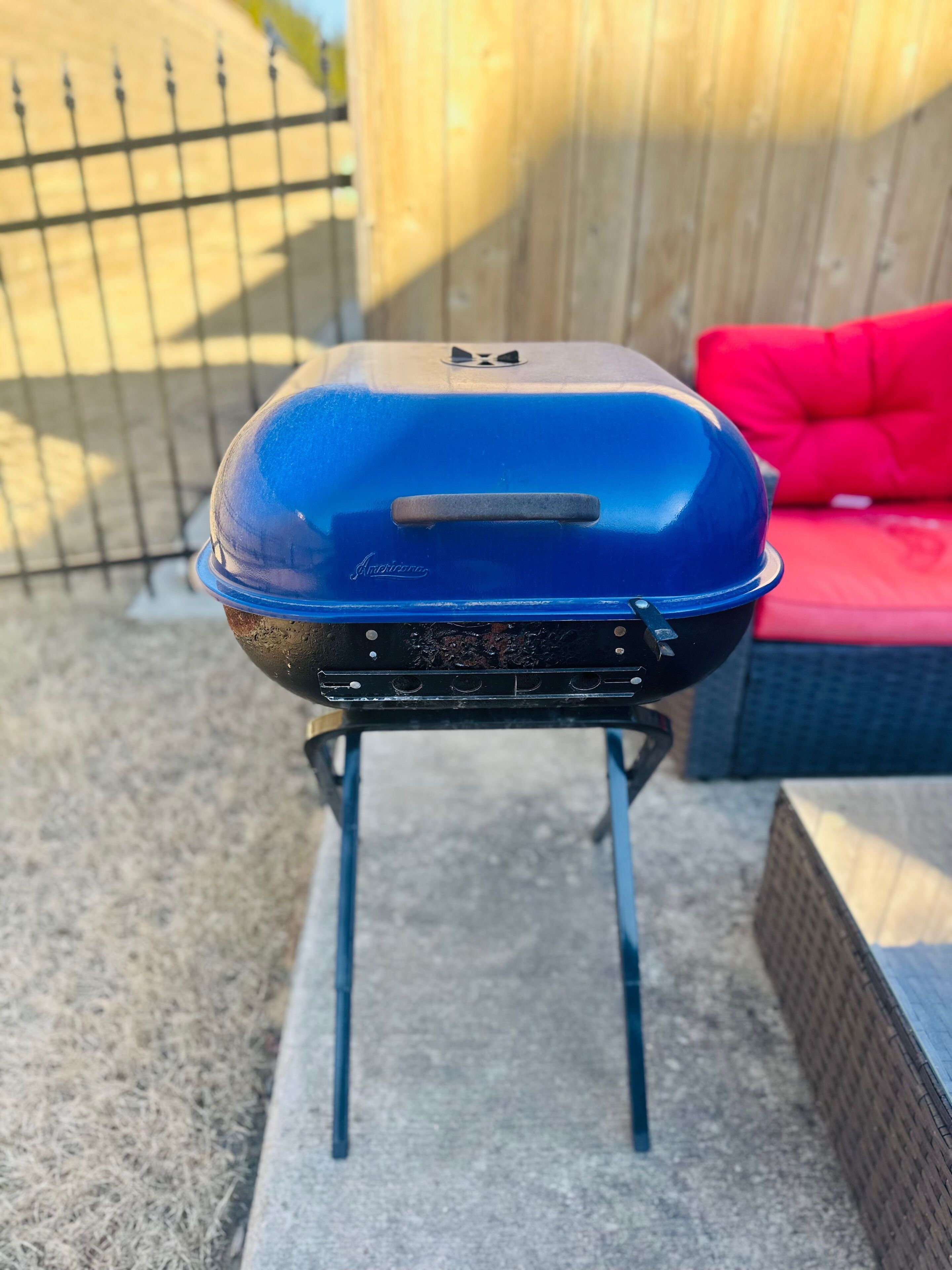Un barbecue portable bleu, doté d’un couvercle, placé sur un support à l’extérieur.