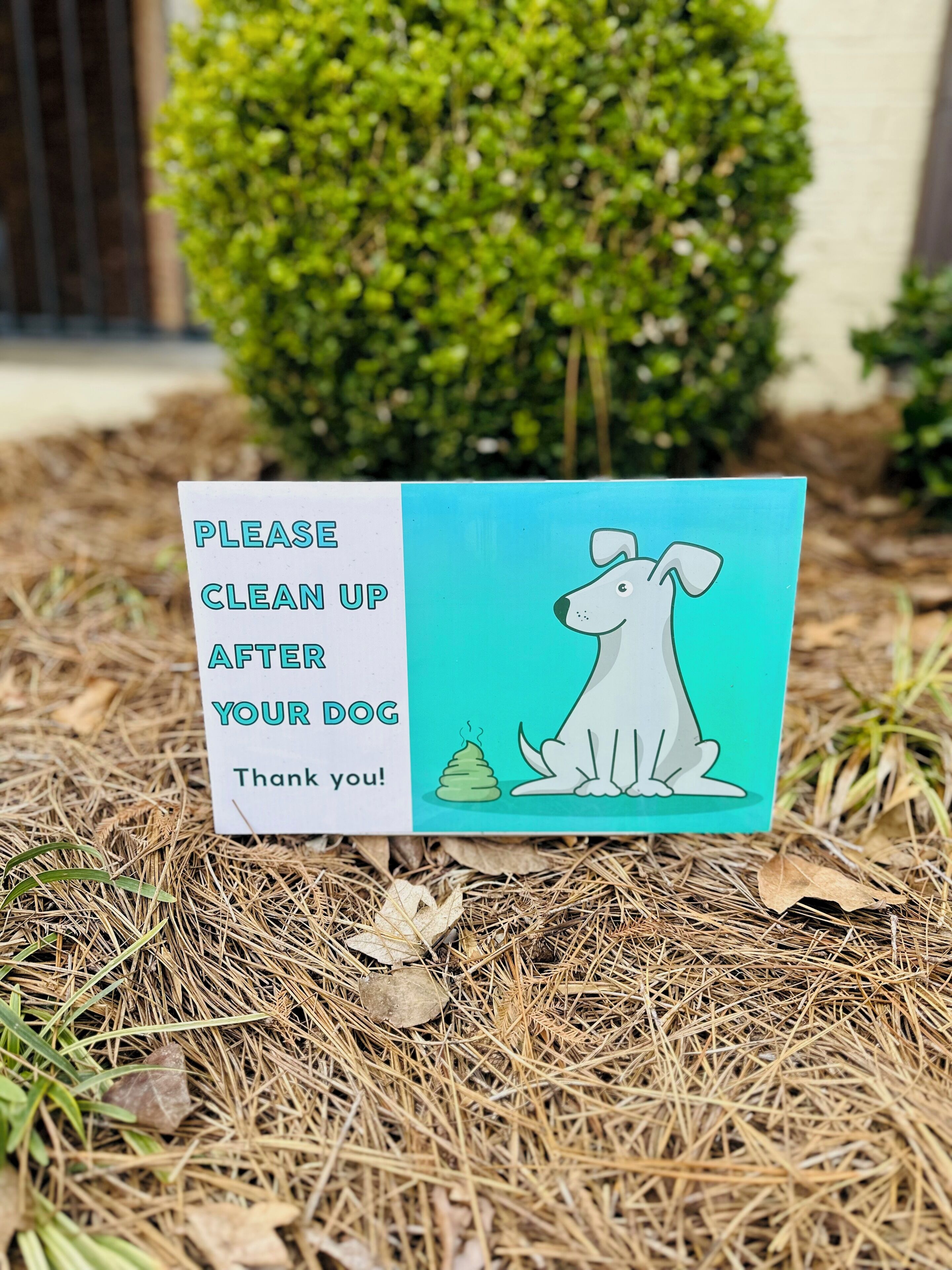 Schild auf einer Wiese mit einer Hundezeichnung und dem Text, Aufforderung zur Reinigung nach Hunden.