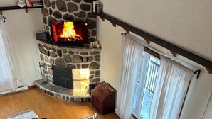 A cozy living room with a stone fireplace, a black sectional sofa, a wooden coffee table, and a floor lamp. - Repère Öra | Spa, ski & nature (Saint-Adolphe-d'Howard)