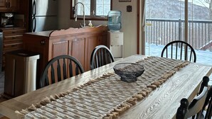 A kitchen with wooden beams, a stainless steel refrigerator, and a dining area with a long table and chairs. - Repère Öra | Spa, ski & nature (Saint-Adolphe-d'Howard)